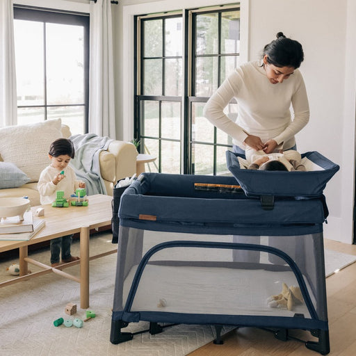 parent stands next to uppababy remi playard usiing the changing station accessory (sold separately)