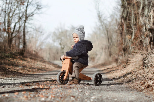 Child shown sitting on bamboo wooden tricycle in fall season on forested path